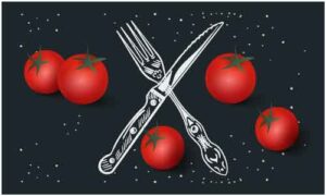 Tomato with knife and fork display on black background